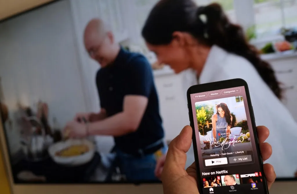 A person with a smartphone showing Meghan’s Netflix series, illustrating public attention